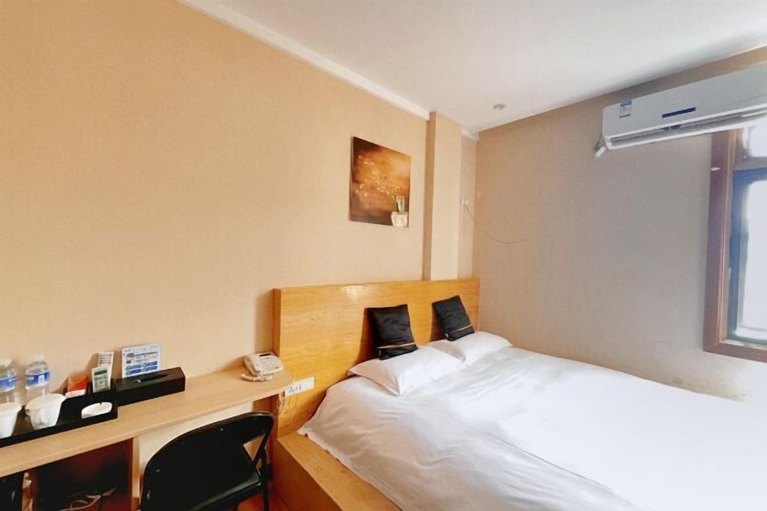 Een hotelkamer met een bed, een bureau met telefoon, een stoel, een kleintje tafeltje met waterflesjes, een koffieapparaat en een wandairconditioner.