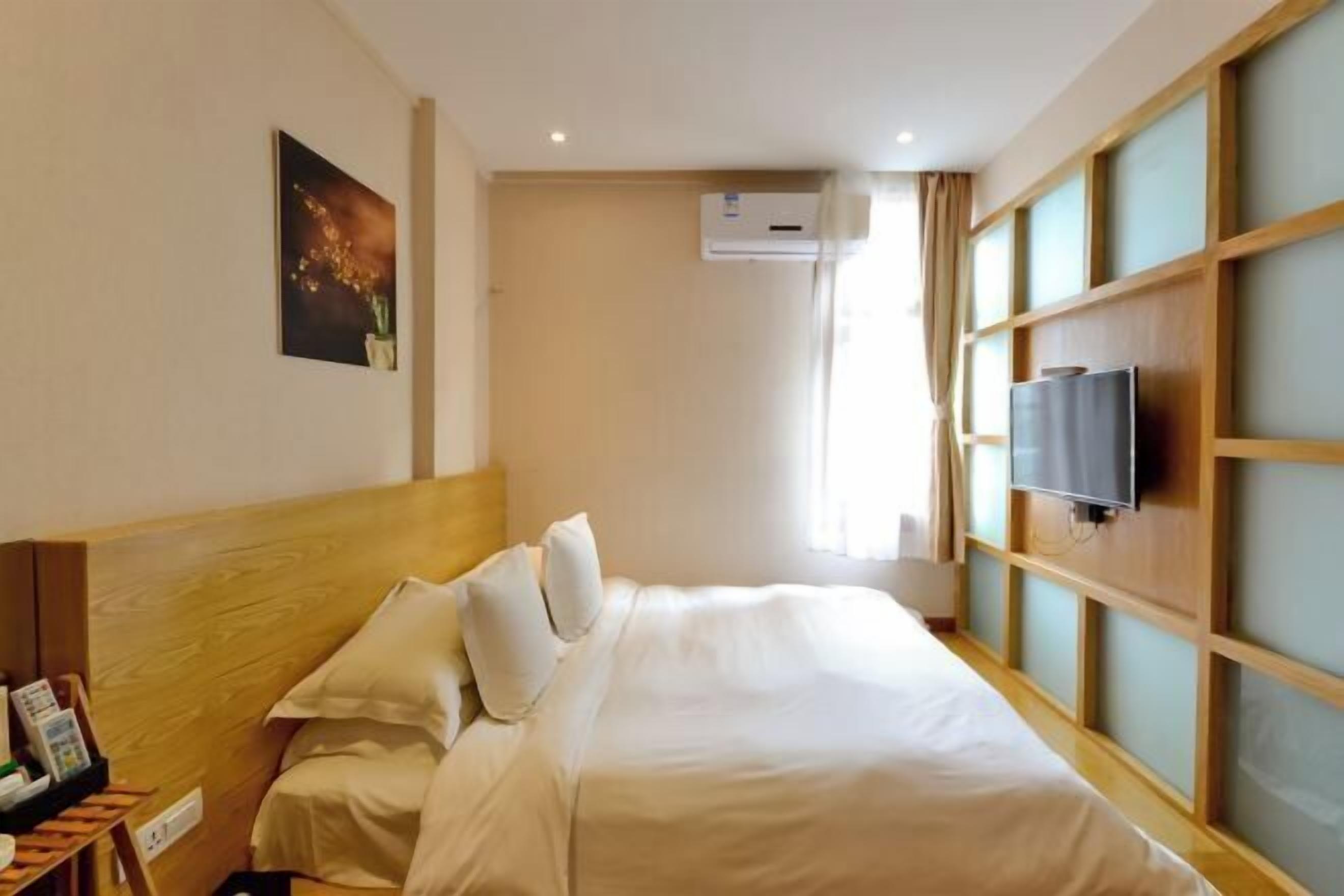 Habitación de hotel con cabecera de madera, cama con ropa blanca, televisor de pantalla plana montado en la pared y aire acondicionado.