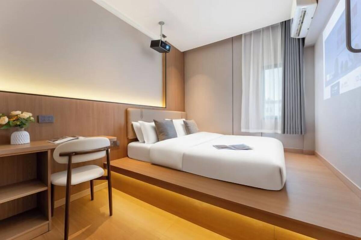 Moderni hotellihuone, jossa on sänky, työpöytä, tuoli ja kattoon asennettu projektori.
