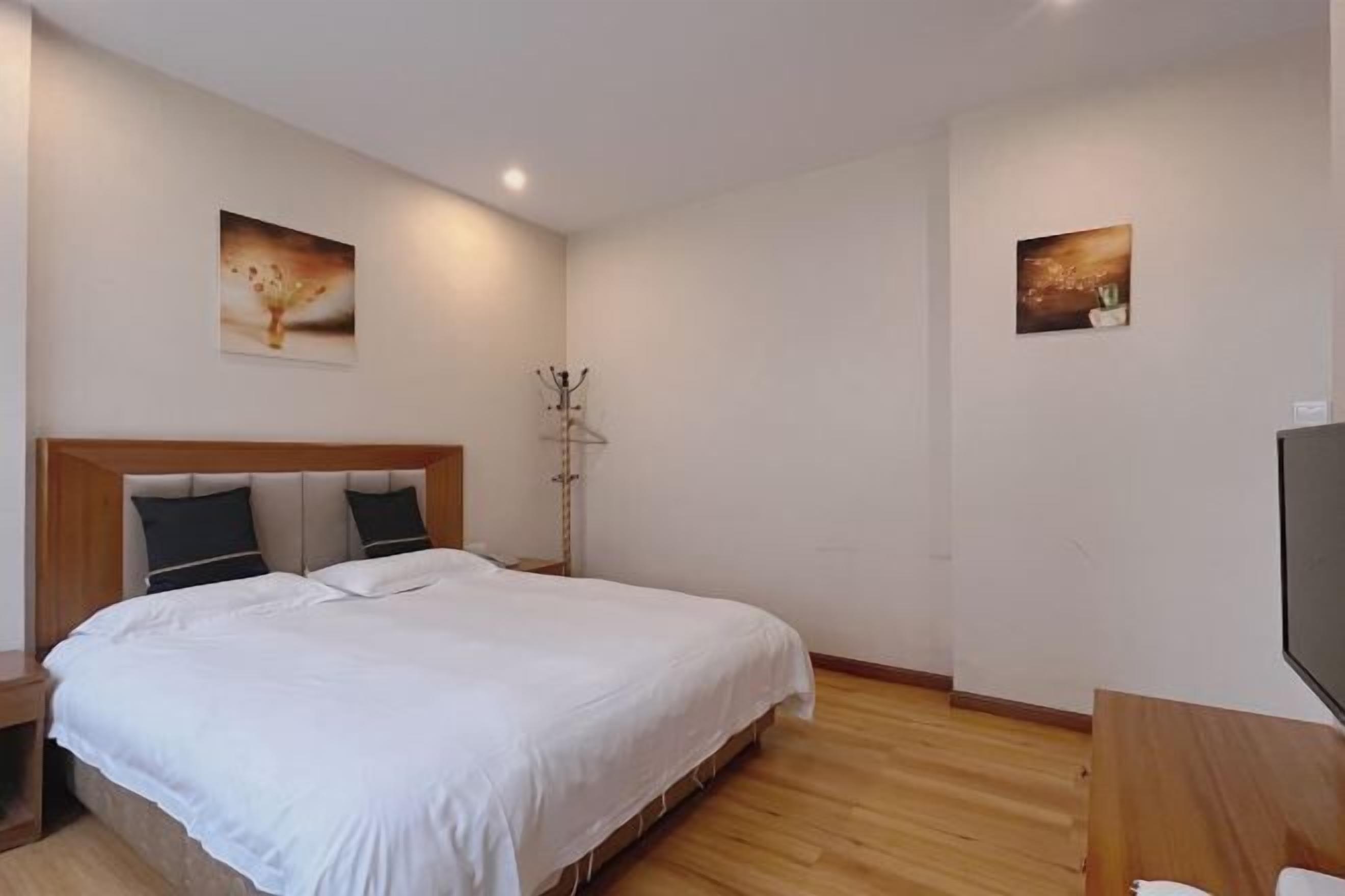 Un dormitorio con una cama grande, cabecero de madera, dos cuadros en la pared, un perchero y un televisor de pantalla plana.