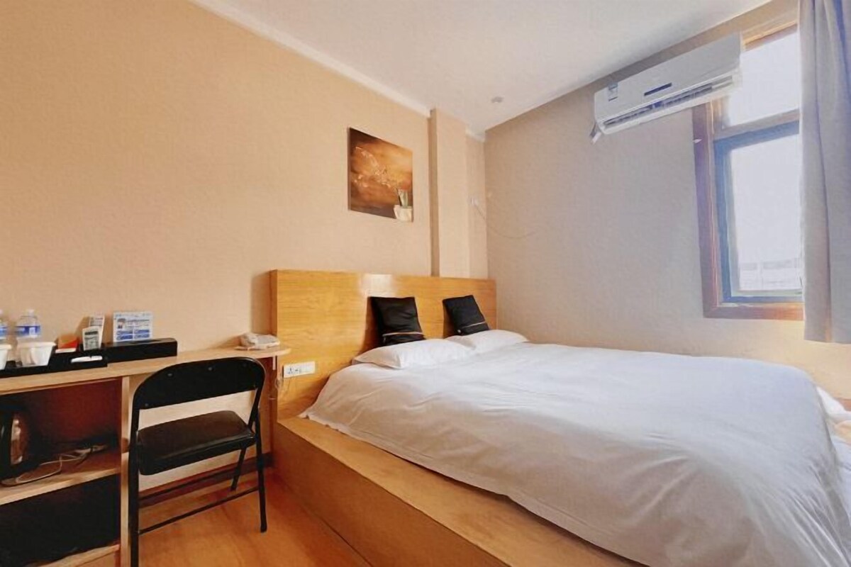 Ein Hotelzimmer mit einem Einzelbett, einem Schreibtisch mit Stuhl, einem kleinen Tisch mit Telefon und einer Klimaanlage.