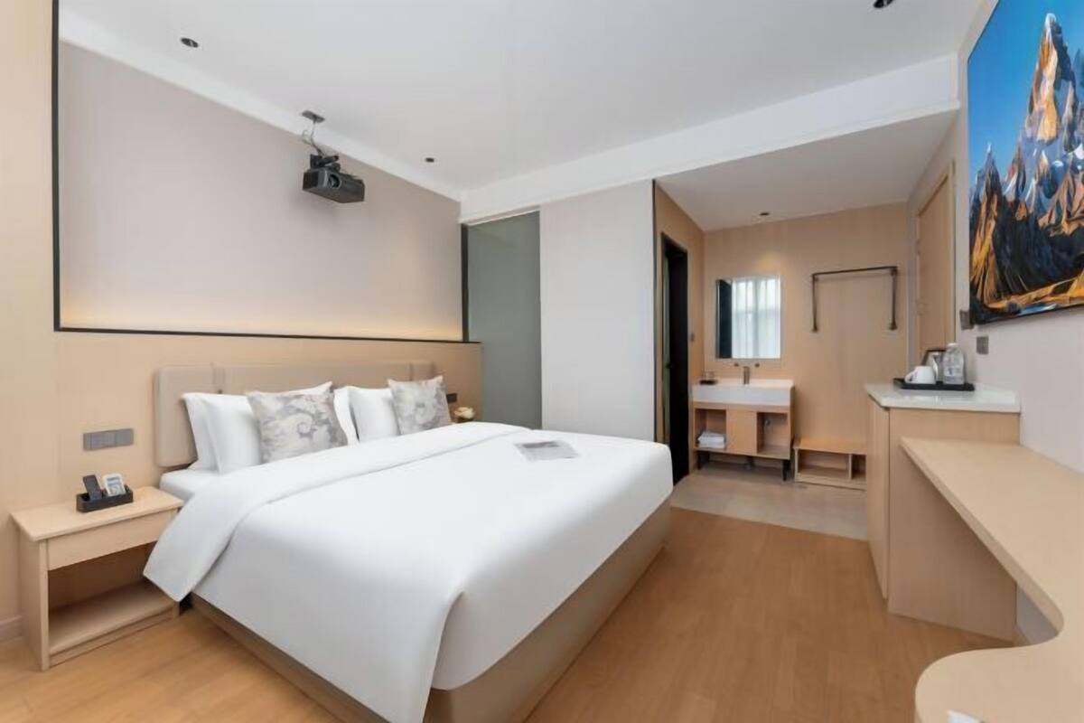 Moderni hotellihuone, jossa on suuri sänky, yöpöytä, jossa on puhelin, työpöytä lampun kanssa, kylpyhuone peilillä ja pesualtaalla sekä taulu seinällä.