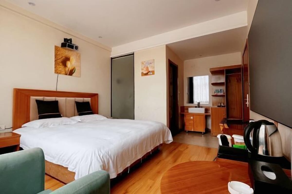 Ein Hotelzimmer mit einem großen Bett, einem Schreibtisch mit Stuhl, einem Kleiderschrank und einem durchgegangenen Tür sichtbaren Badezimmer.