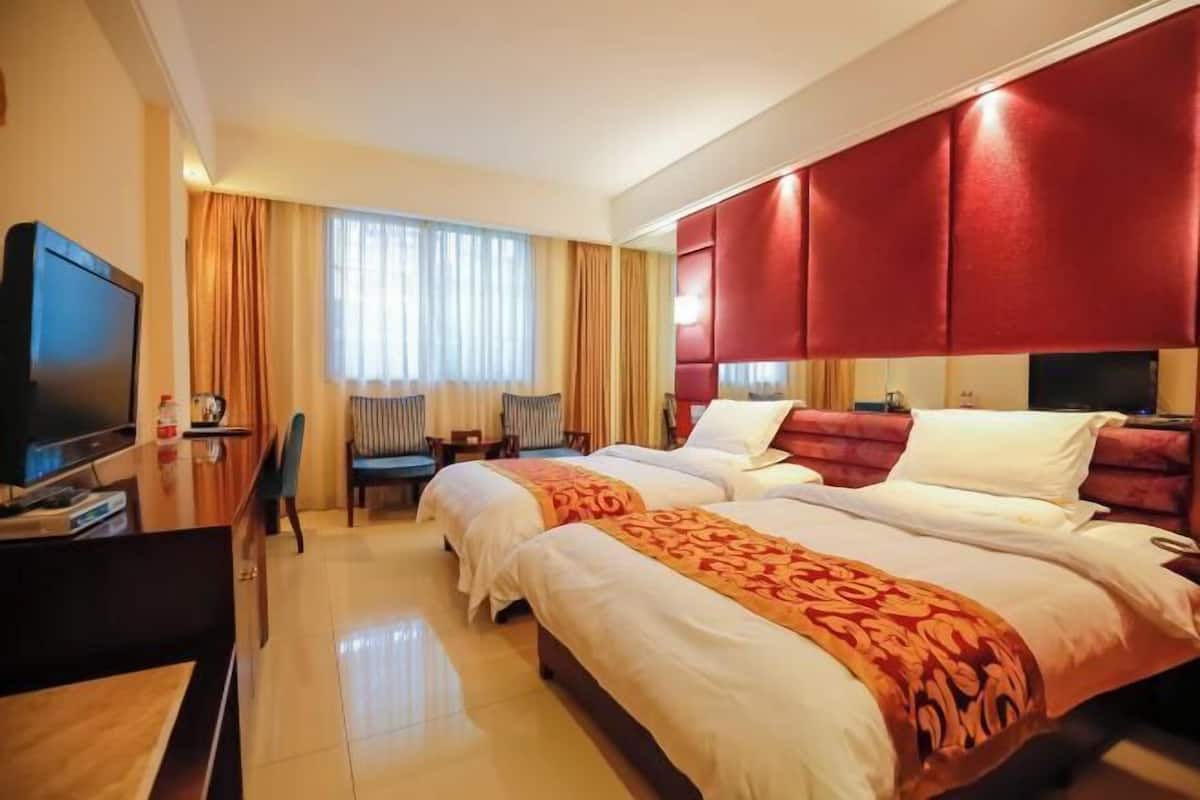 Een hotelkamer met twee bedden, een televisie, een bureau en een raam met gordijnen.