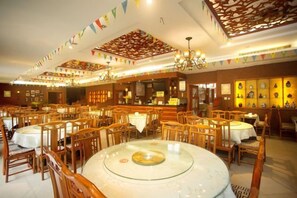 Een restaurant met ronde tafels, houten stoelen en een centrale glazen tafel.