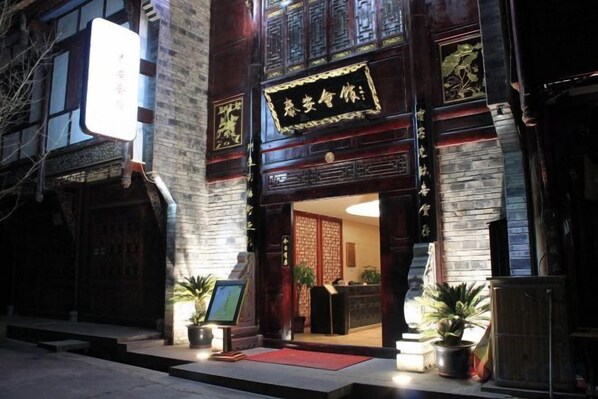 A traditional building with a signboard, a reception desk, and potted plants outside.