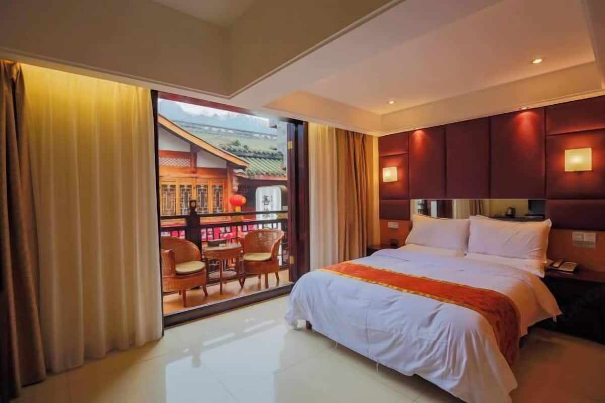 Een hotelkamer met een bed, een bureau, een stoel en uitzicht op een traditioneel gebouw door een glazen deur.