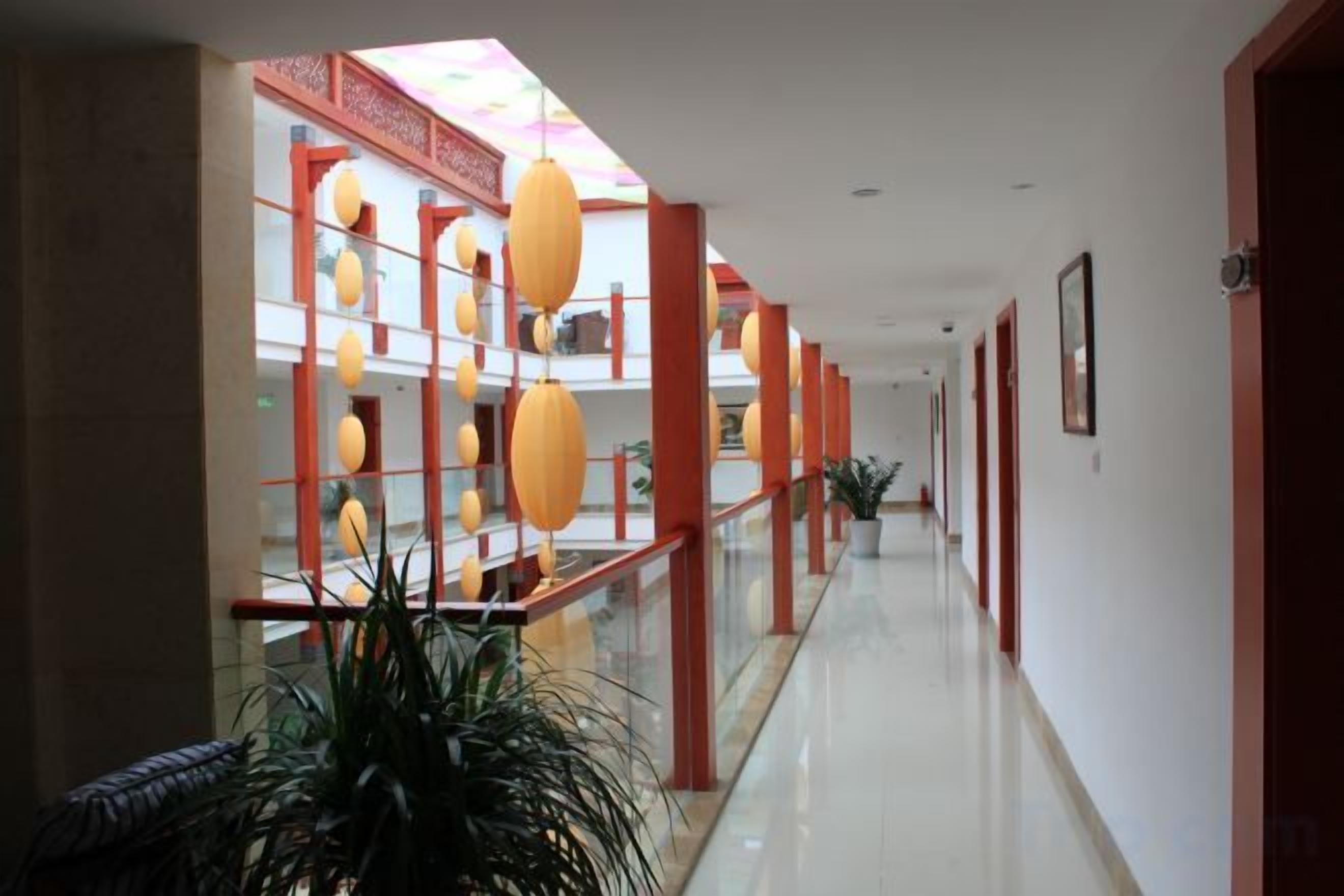 A long corridor with a glass railing, red structural columns, and hanging spherical lights.