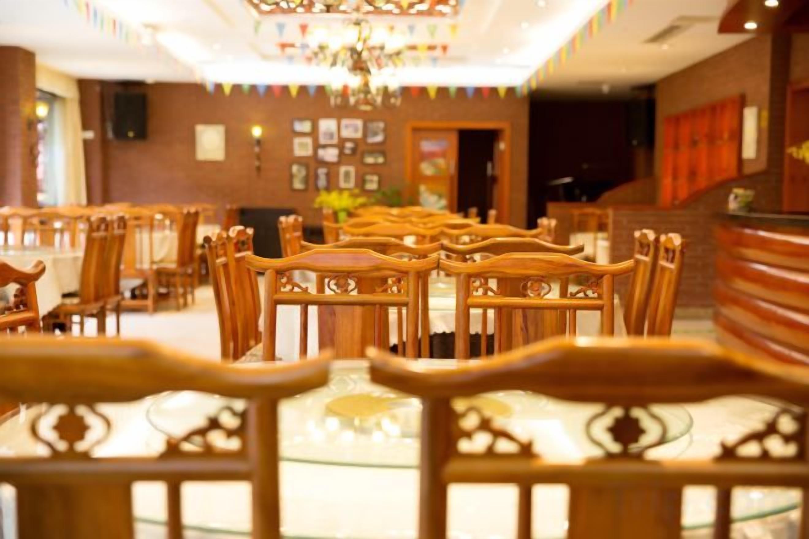 A hotel dining area with rows of wooden tables and chairs, a chandelier, and a reception desk.