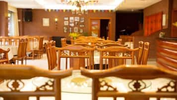 A hotel dining area with rows of wooden tables and chairs, a chandelier, and a reception desk.