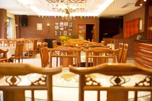 Ein Hotel-Essbereich mit Reihen aus Holztischen und -stühlen, einer Kristallleuchtre und einer Rezeption.