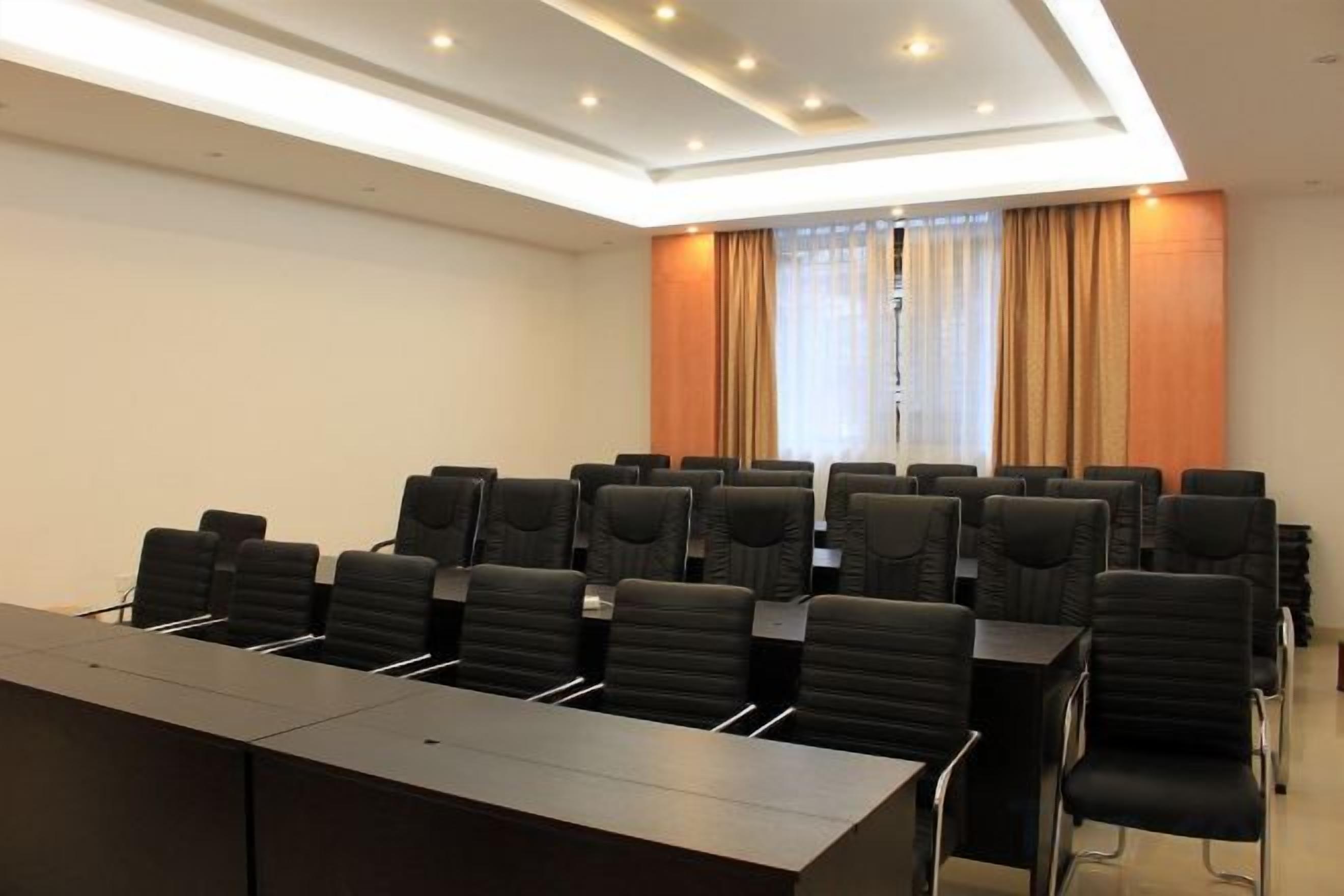 Una sala de conferencias con una larga mesa y numerosas sillas, una ventana con cortinas e iluminación empotrada en el techo.