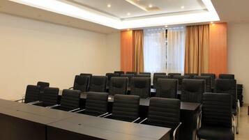 Una sala de conferencias con una larga mesa y numerosas sillas, una ventana con cortinas e iluminación empotrada en el techo.