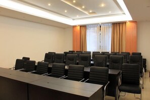 Une salle de conférence avec une longue table et de nombreuses chaises, une fenêtre avec des rideaux et un plafond doté d’un éclairage encastré.
