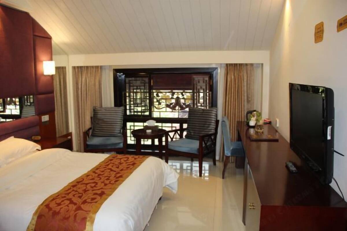Een hotelkamer met een groot bed, een televisie, een bureau met stoel, en een balkon met uitzicht.