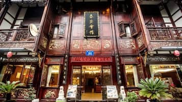 A traditional building with ornate woodwork, a signboard, and potted plants at the entrance.