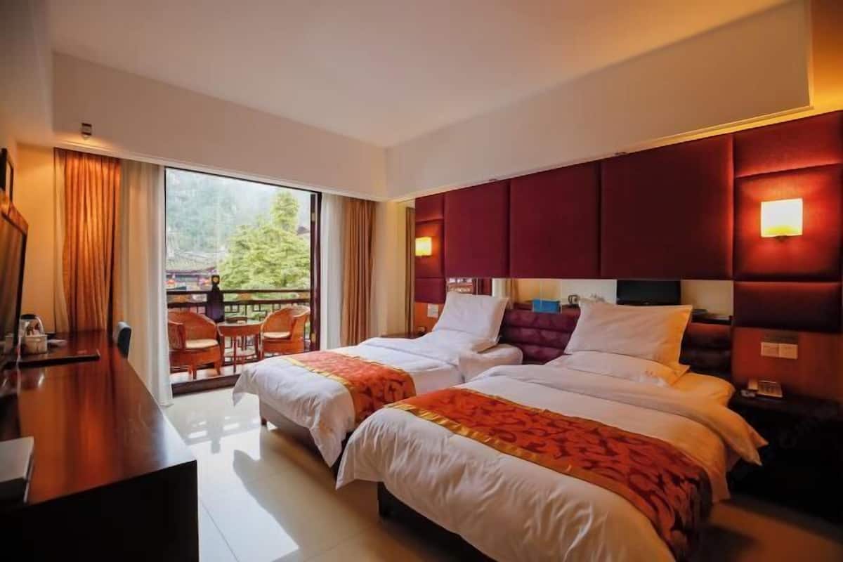 Een hotelkamer met twee bedden, een bureau en een balkon met stoelen.