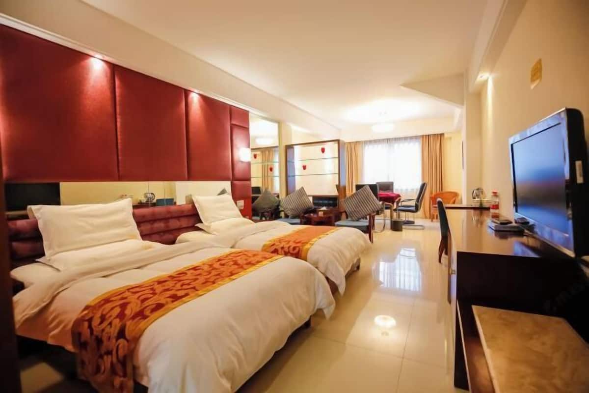 Een hotelkamer met twee bedden, een bureau, een televisie en een zithoek met stoelen en een tafel.