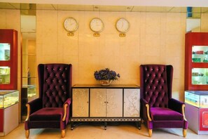 Een hal met twee paarse fauteuils, een console tafel in het midden met een plant erop, en drie wandklokken.