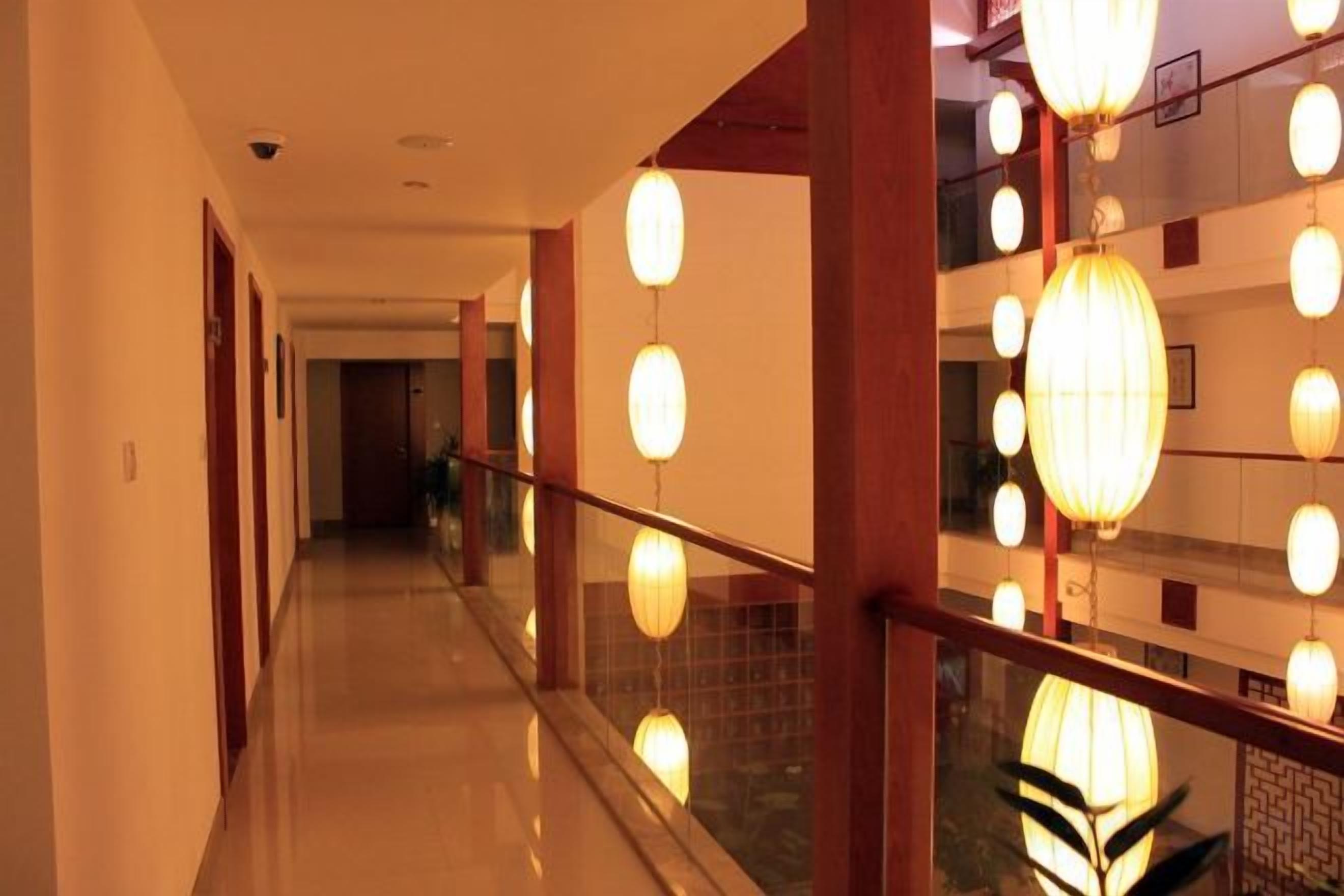 A corridor with a glass railing, hanging lights, and a view of a building's interior.