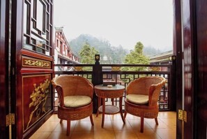 Ein Balkon mit Korbstühlen und einem kleinen Tisch, mit Blick auf ein traditionelles Gebäude und Bäume.