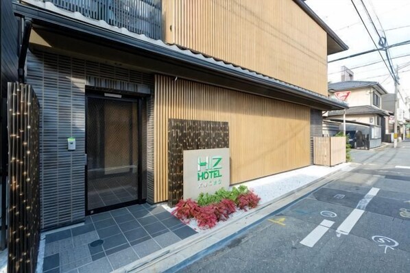 A hotel with a closed entrance, a signboard, and a small garden area with red flowers.