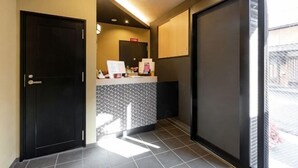 Een hotel receptie met een balie, een zwarte deur, een grote spiegel en uitzicht door een glazen deur.