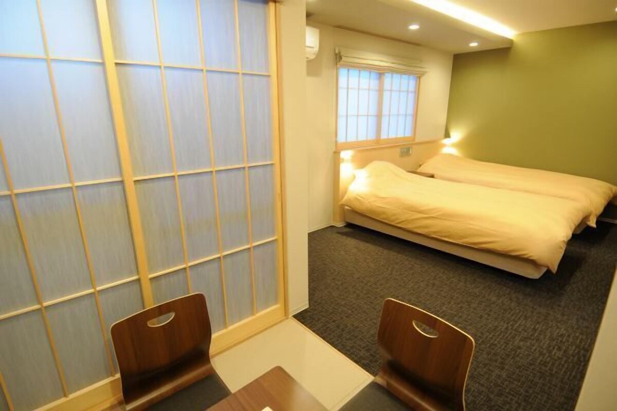 A hotel room with two beds, a sliding shoji screen, a small table, and a chair.