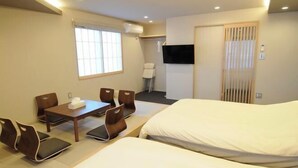 Een hotelkamer met een bed, een tafel met stoelen, een aan de muur bevestigde televisie en een raam met zonwering.