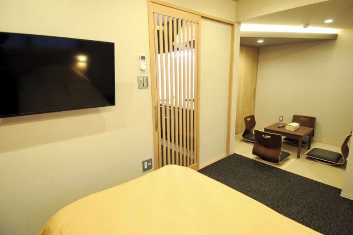 A hotel room with a bed, a TV mounted on the wall, a desk with a chair, and a sliding door.