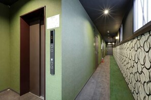 Un couloir avec un ascenseur, un panneau de commande fixé au mur et un mur décoré de motifs.