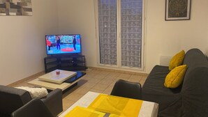 A living room with a television, a sofa with yellow cushions, a coffee table, and a sliding glass door.
