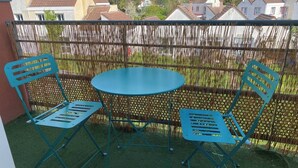 A balcony with a round table and two chairs, a bamboo fence, and houses in the background.