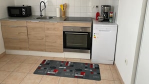 A compact kitchen with wooden cabinets, a microwave, an oven, a coffee maker, and a small refrigerator.