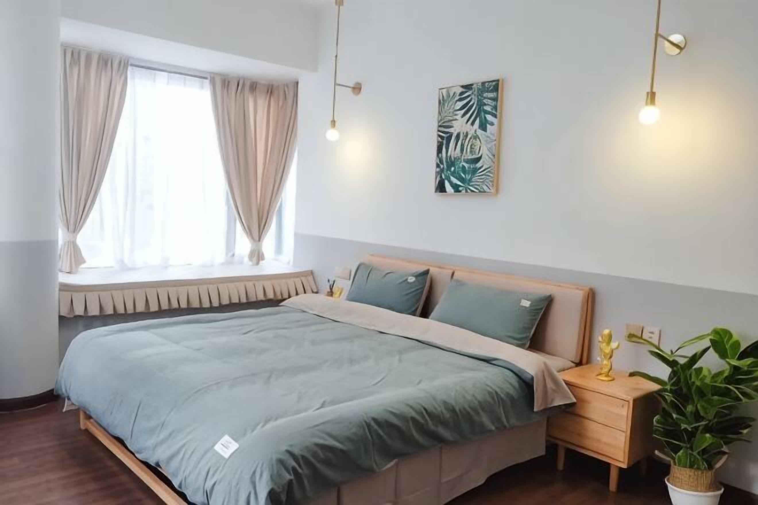 A bedroom with a bed, a nightstand, a potted plant, and a window with curtains.