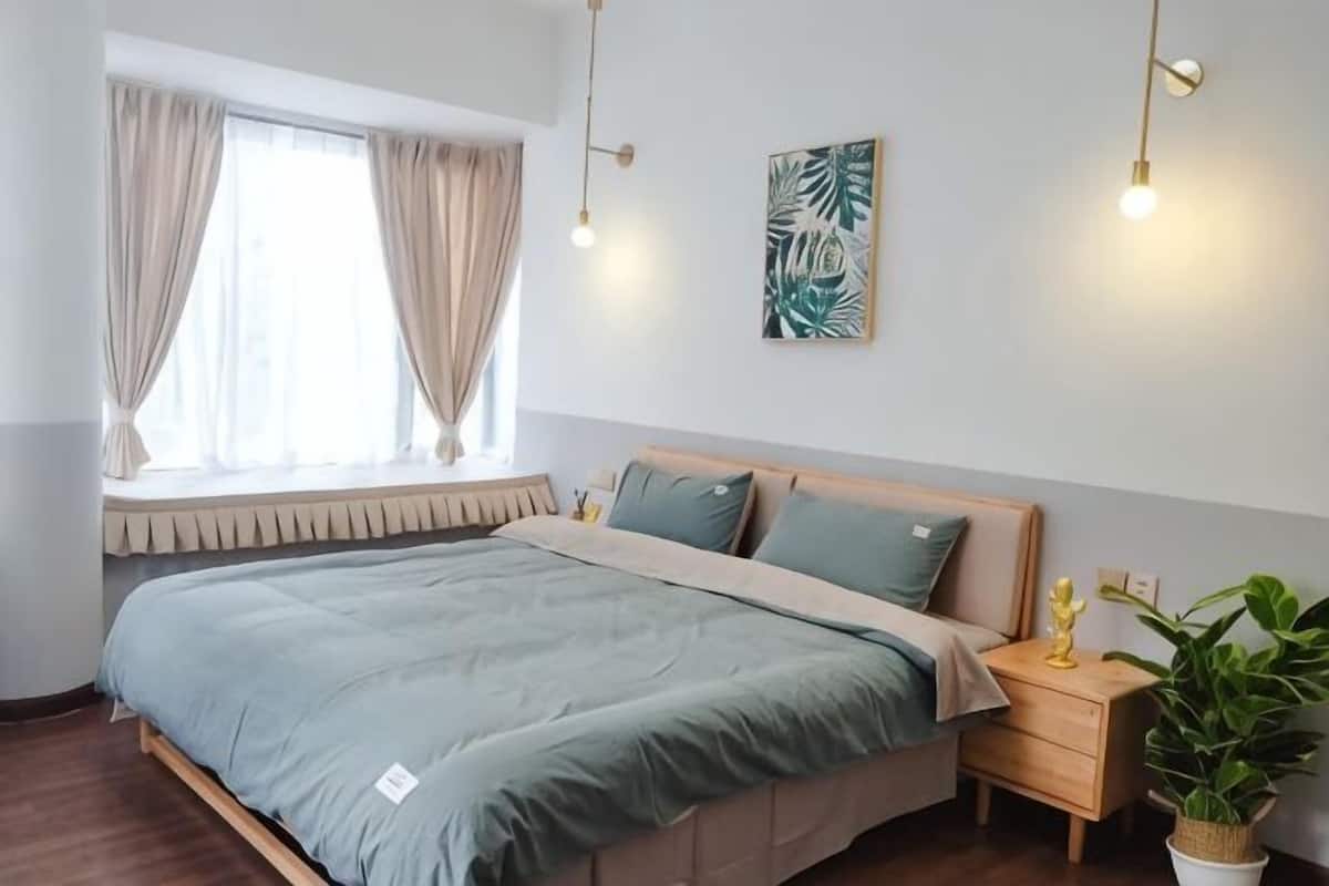 Un dormitorio con cama, mesita de noche, planta en maceta y ventana con cortinas.