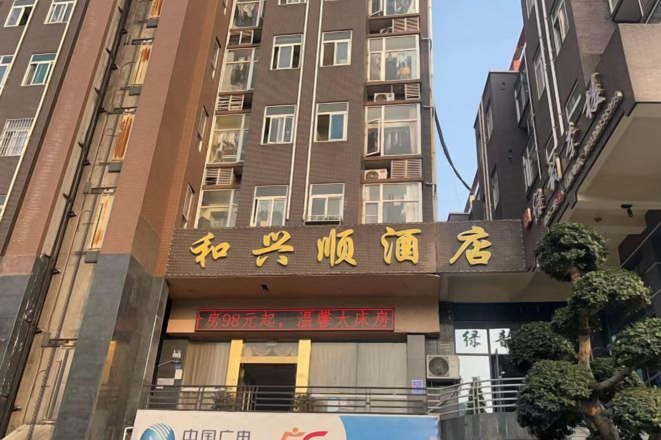 A hotel with a sign in Chinese characters, multiple floors, and a tree in front.