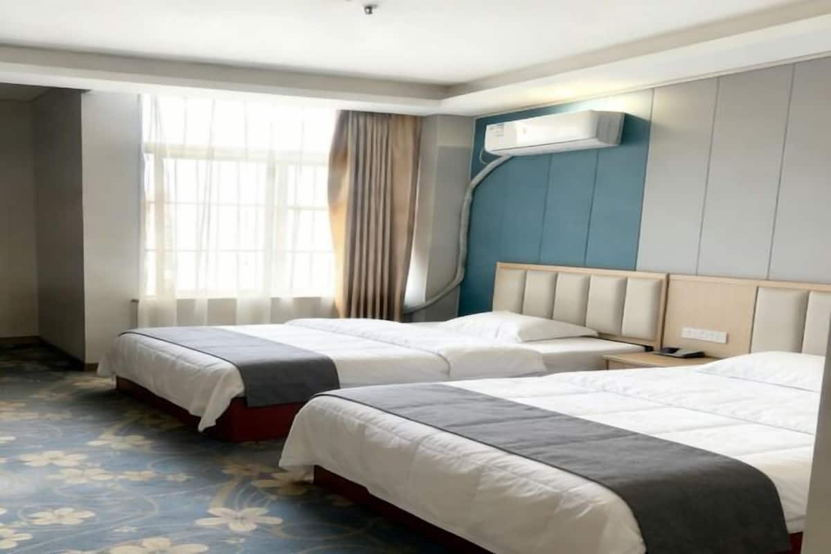 A hotel room with two beds, a window with curtains, an air conditioning unit, and a floral carpet.