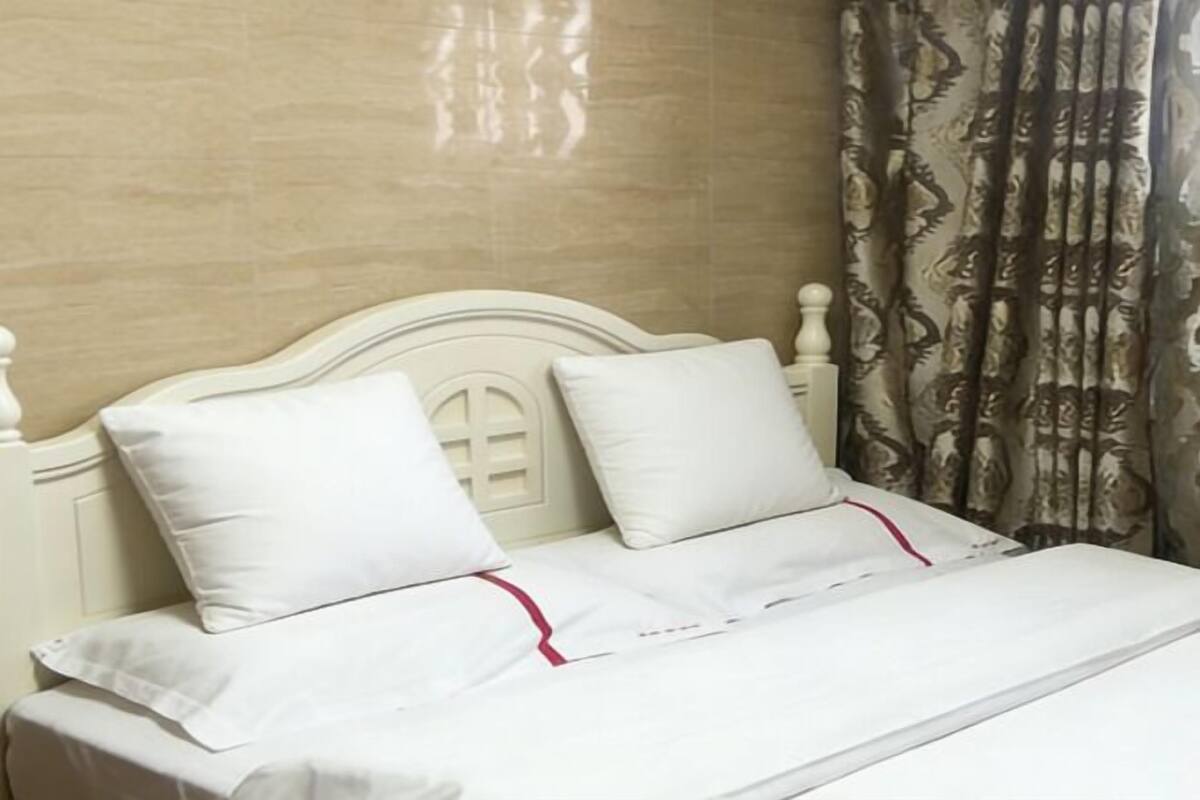 A bed with white bedding and a red trim, a headboard with a decorative design, and a patterned curtain in the background.