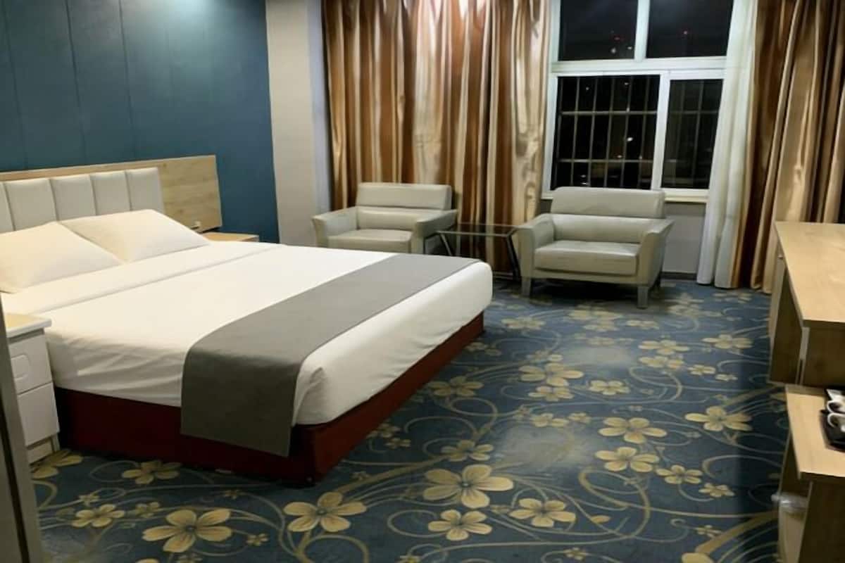A hotel room with a bed, two chairs, a small table, and a window with curtains.