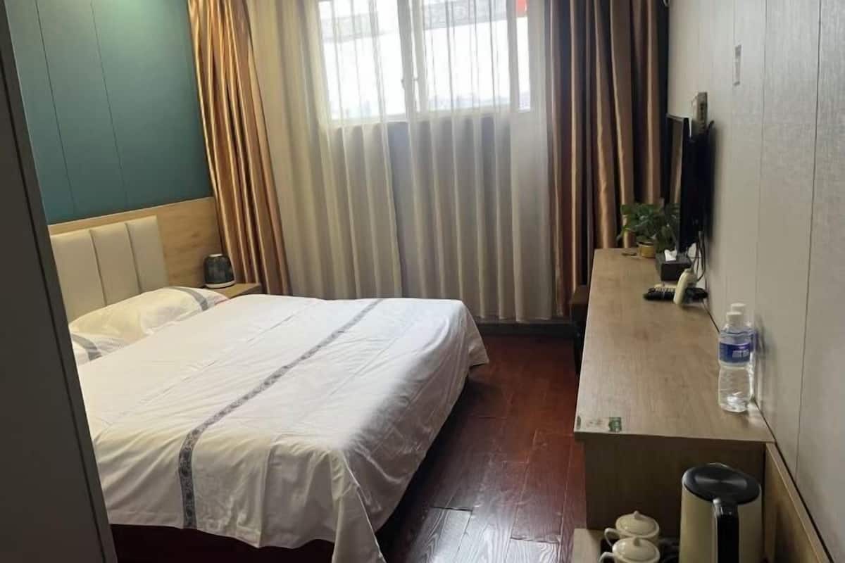 A hotel room with a bed, a desk with a chair, a TV, and a window with curtains.