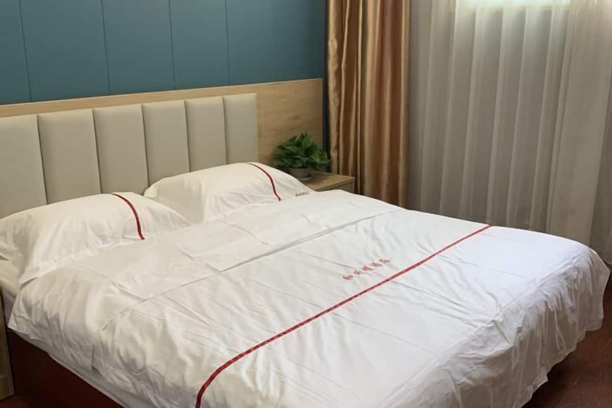 A neatly made bed with a white bedspread and red trim, a wooden headboard, and a small plant on the nightstand.