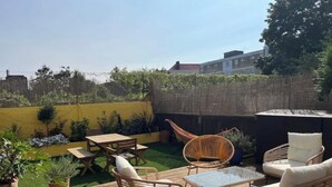Terraza de madera con mobiliario exterior, una mesa y plantas en macetas.
