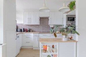 A modern kitchen with white cabinets, a wooden countertop, and two pendant lights. - Scandi Style Maisonette with Garden, Shoreditch (London)