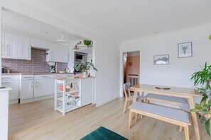 Een moderne keuken met witte kasten, een tegelwand van baksteen en een centraal eiland met een spoelbak en opbergruimte.
