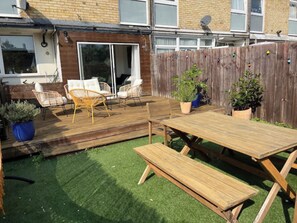 Een achtertuin met een houten terras, tuinmeubels en potplanten.