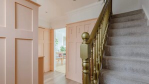 Una escalera con barandilla que lleva a un rellano, una puerta con paneles y vista a una habitación con una mesa y sillas.