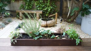 Een tuin met verhoogde borders, een houten bankje en een rustieke waterpartij.