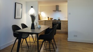 Een moderne eetruimte met een houten tafel en stoelen, een vaas met bloemen en een keuken op de achtergrond.