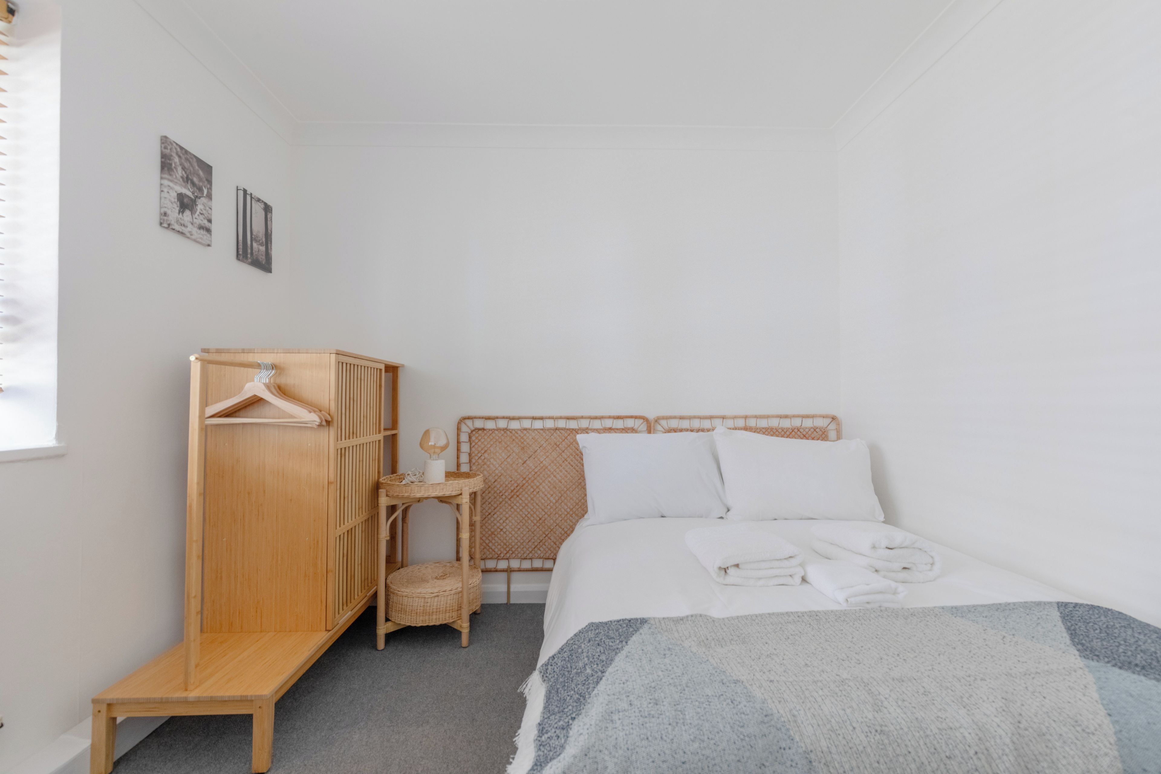A bedroom with a bed, a wooden wardrobe, a small table with a lamp, and a wall-mounted shelf.